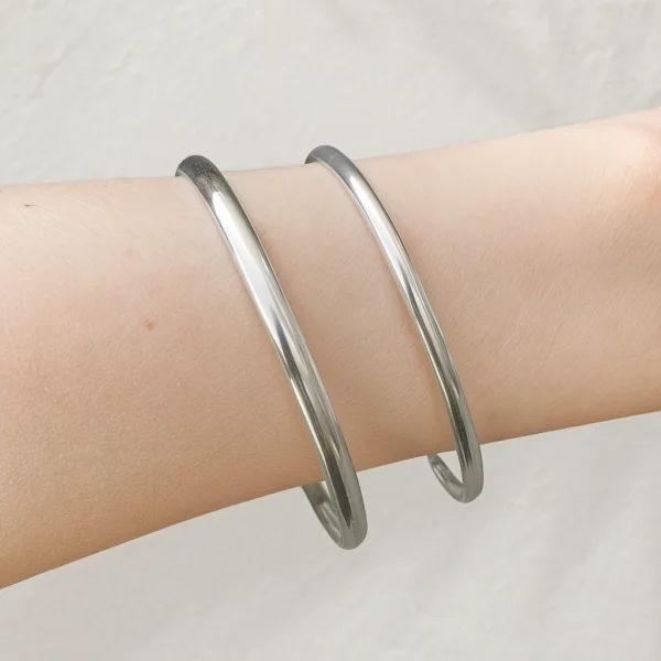 Twee zilveren bangles met dopsluiting om een vrouwelijke pols, strak en minimalistisch ontworpen